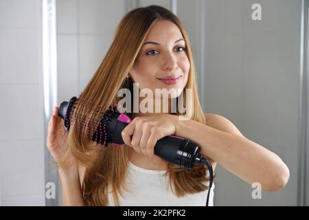 Die junge Frau hält einen runden Bürstenfon, um das Haar zu Hause auf einfache Weise zu stylen Stockfoto