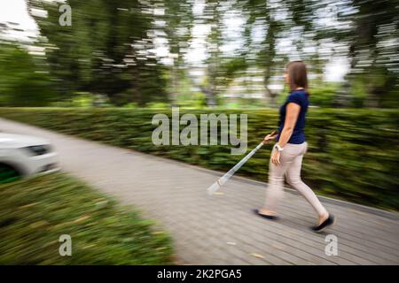 Blinde Frau, die mit ihrem weißen Stock auf den Straßen der Stadt unterwegs ist Stockfoto