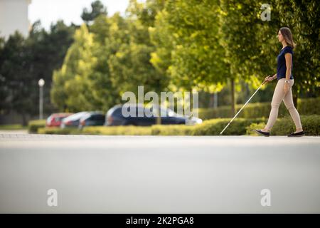 Blinde Frau, die auf den Straßen der Stadt geht, mit ihrem weißen Stock, um den städtischen Raum besser zu navigieren und sicher an ihr Ziel zu gelangen Stockfoto