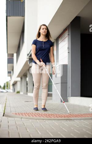 Blinde Frau, die mit ihrem weißen Stock auf den Straßen der Stadt unterwegs ist Stockfoto