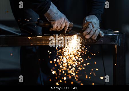 Mann, der mit Schleifmaschine an Eisen arbeitet. Mann bei der Arbeit. Funkelt und Feuer vom Schneiden der Mühle. Mahlwerk. Arbeiter. Stockfoto