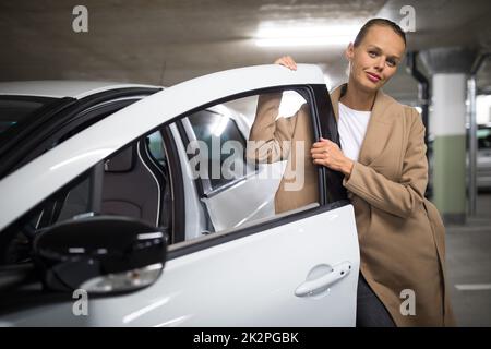 Tiefgarage (flaches, farbiges Bild des DOF) - eine junge Frau mit ihrem Auto in der Tiefgarage Stockfoto