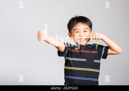 Kleiner süßer Junge, 5-6 Jahre alt, lächelt Zähne putzen und zeigt Daumen hoch, um ein gutes Zeichen zu geben Stockfoto