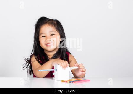 Ein kleines süßes Mädchen im Alter von 3-4 Jahren lächelt mit einem Bleistiftspitzer, während es Hausaufgaben im Studio Einzelaufnahme macht Stockfoto