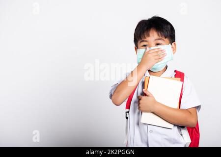 Asiatischer Schüler Junge trägt Thai Uniform und medizinische Gesichtsmaske und Hand-Abdeckung Mund Stockfoto