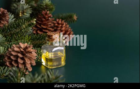 Glasflasche mit ätherischem Koniferöl in der Nähe von Tannenzweigen und Kiefernzapfen auf grünem Nahbild Stockfoto