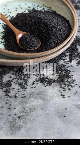 Teller mit indischem Gewürz Schwarzer Kreuzkümmel (Nigella sativa oder Kalonji), Nahaufnahme mit einem Holzlöffel Stockfoto