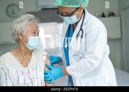 Ältere asiatische ältere Frau, die Gesichtsmaske trägt, erhält von einem Arzt eine Covid-19- oder Coronavirus-Impfung. Stockfoto