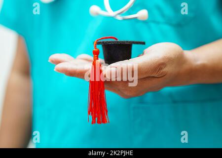 Asiatische Frau Arzt hält Abschlusshut im Krankenhaus, Medizinische Ausbildung Konzept. Stockfoto