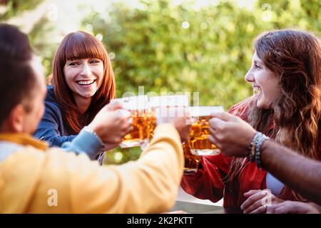 Gruppe von Freunden toasten mit einem Glas Bier - Millennials haben gemeinsam Spaß im Bierrestaurant im Freien - Junge Männer und Frauen glücklich zusammen lif Stockfoto