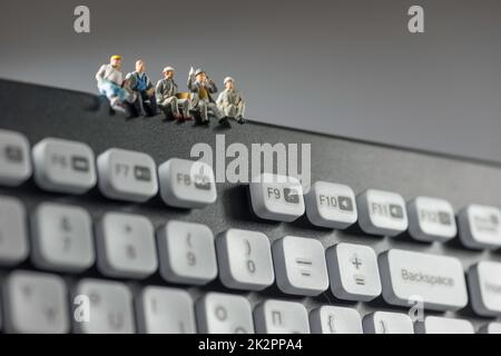 Miniaturarbeiter, die auf der Tastatur sitzen. Technologiekonzept Stockfoto