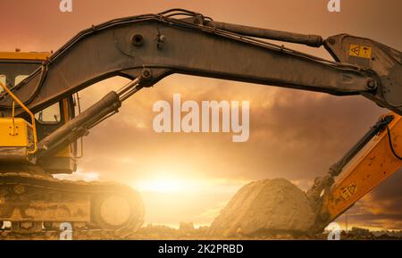 Baggerlader auf der Baustelle geparkt, nachdem Boden gegraben wurde. Bulldozer auf Sonnenuntergang Himmel und Wolken Hintergrund. Bagger nach der Arbeit. Erdbewegungsmaschine auf der Baustelle in der Dämmerung. Bagger mit Schmutzbehälter. Stockfoto