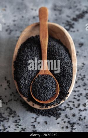 Indisches Gewürz Schwarze Kreuzkümmel (Nigella sativa oder Kalonji) Samen in Schüssel mit Löffel auf hölzernem Tisch. Stockfoto