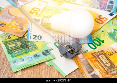 Elektrischer Stecker und Glühbirne auf Euro-Banknoten Stockfoto