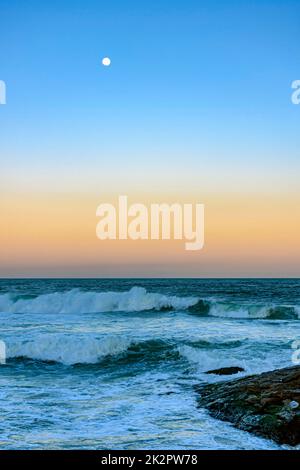 Mond über dem Meer und Wellen bei Sonnenuntergang Stockfoto