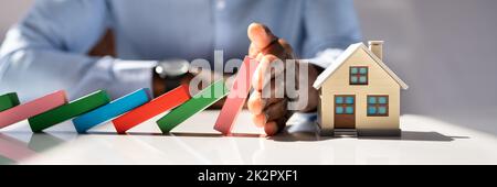 Geschäftsmann, Der House Model Vor Herunterfallenden Holzblöcken Beschützt Stockfoto