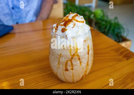 Der hölzerne Tisch bietet einen Blick auf ein Glas Kaffeefrasten mit Karamellfüllung Stockfoto