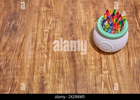 Ein niedlicher runder weißer und türkisfarbener Keramikhalter mit einer Nautilus-Schale auf der Vorderseite. Gefüllt mit bunten Buntstiften auf einem Holzschreibtisch. Stockfoto