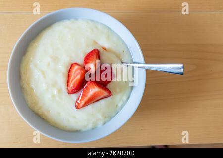 Viele geschnittene Erdbeeren mit Reispudding in der Schüssel sind bereit zum Essen mit Silberlöffel oder als köstliches Fingerfood und gesunde Snacks mit roten Früchten und Vitaminen auf einem hölzernen Küchentisch für nachhaltige Nüsse Stockfoto