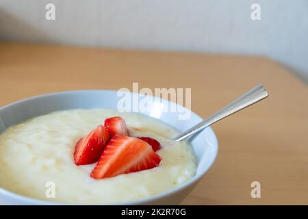 Viele geschnittene Erdbeeren mit Reispudding in der Schüssel sind bereit zum Essen mit Silberlöffel oder als köstliches Fingerfood und gesunde Snacks mit roten Früchten und Vitaminen auf einem hölzernen Küchentisch für nachhaltige Nüsse Stockfoto