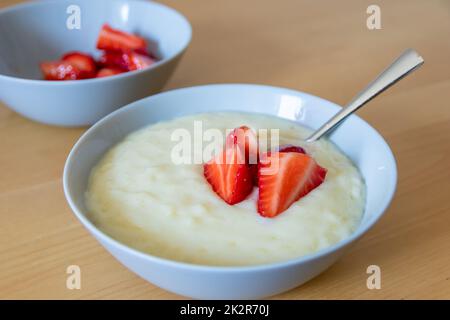 Viele geschnittene Erdbeeren mit Reispudding in der Schüssel sind bereit zum Essen mit Silberlöffel oder als köstliches Fingerfood und gesunde Snacks mit roten Früchten und Vitaminen auf einem hölzernen Küchentisch für nachhaltige Nüsse Stockfoto