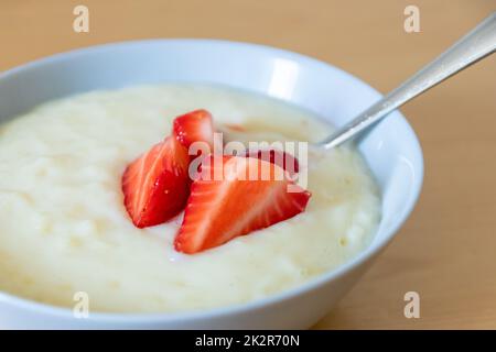 Viele geschnittene Erdbeeren mit Reispudding in der Schüssel sind bereit zum Essen mit Silberlöffel oder als köstliches Fingerfood und gesunde Snacks mit roten Früchten und Vitaminen auf einem hölzernen Küchentisch für nachhaltige Nüsse Stockfoto