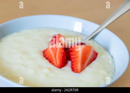 Viele geschnittene Erdbeeren mit Reispudding in der Schüssel sind bereit zum Essen mit Silberlöffel oder als köstliches Fingerfood und gesunde Snacks mit roten Früchten und Vitaminen auf einem hölzernen Küchentisch für nachhaltige Nüsse Stockfoto