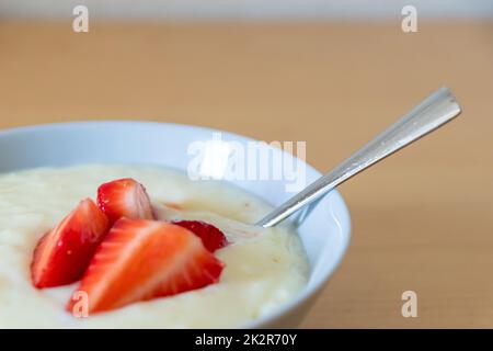 Viele geschnittene Erdbeeren mit Reispudding in der Schüssel sind bereit zum Essen mit Silberlöffel oder als köstliches Fingerfood und gesunde Snacks mit roten Früchten und Vitaminen auf einem hölzernen Küchentisch für nachhaltige Nüsse Stockfoto