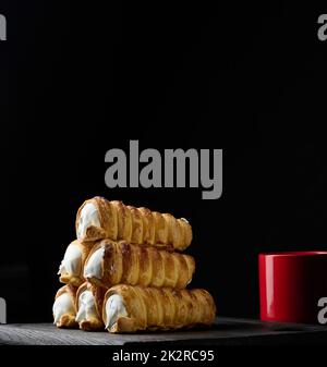 Gebackene Tubuli gefüllt mit geschlagener Eiweiß-Creme auf einem schwarzen Küchenbrett aus Holz Stockfoto