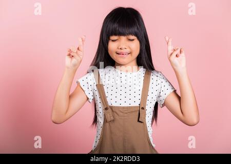 Ein asiatisches kleines Kind im Alter von 10 Jahren lächelt mit den Fingern und schließt die Augen Stockfoto