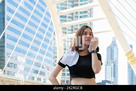 Junge Sportlerin in Sportbekleidung im Stehen und schweißabwischen nach Laufen oder Workout in der Stadt. Stockfoto