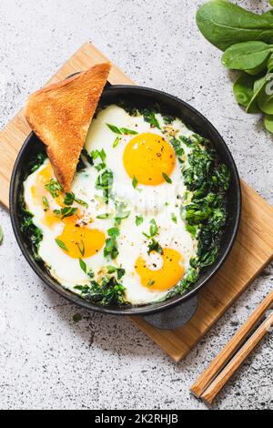Grüner Shakshuka in einer gusseisernen Pfanne. Spiegeleier mit Spinat und gebratenem Toast. Gesundes, nahrhaftes Frühstück Stockfoto