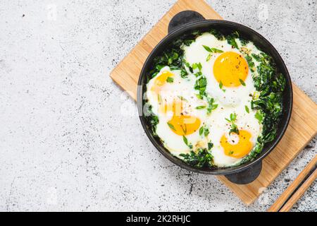 Grüner Shakshuka in einer gusseisernen Pfanne. Spiegeleier mit Spinat und gebratenem Toast. Gesundes, nahrhaftes Frühstück Stockfoto