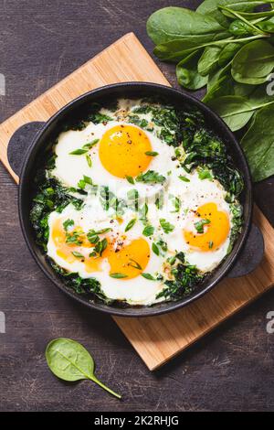 Grüner Shakshuka in einer gusseisernen Pfanne. Spiegeleier mit Spinat und gebratenem Toast. Gesundes, nahrhaftes Frühstück Stockfoto