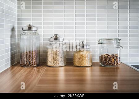 Küchencontainer und Lebensmittel in Gläsern. Inhaltsstofforganisation und nachhaltige Lagerung. Pasta, Haferflocken, Reis und Müsli. Nahaufnahme des Holztisches. Stockfoto