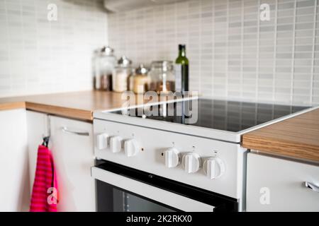 Küche mit Herd, Backofen und Tisch. Schrank-Design in kleinen Haus. Induktionsherd aus elektrischer Keramik. Moderne einrichtung in skandinavischem Weiß. Stockfoto