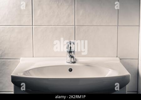 Waschbecken im Badezimmer. Wasserhahn, Wasserhahn und Waschbecken. Dramatisches launisches Licht mit dunklen Schatten. Öffentliche Toilette. Dreckige, rustikale oder dreckige alte Toilette. Stockfoto