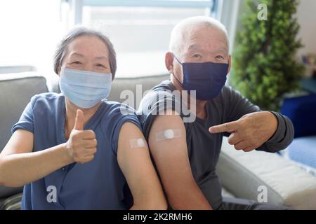 Seniorenpaar mit Gesichtsmaske Virenschutz und Verbandspritze covid-19 geimpft mit Daumen nach oben Stockfoto