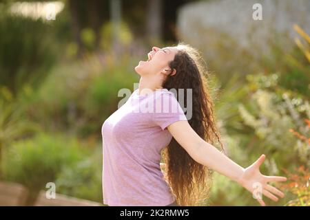 Aufgeregte Frau, die Arme ausstreckt und in einem Park schreit Stockfoto