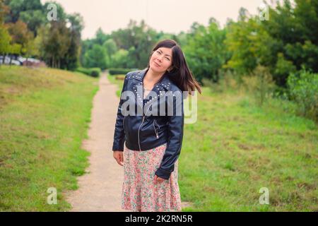 Eine schöne Frau mit schwarzen langen Haaren steht auf einem Pfad im Park. Stockfoto