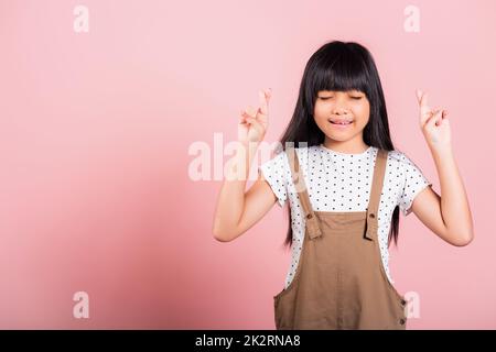 Ein asiatisches kleines Kind im Alter von 10 Jahren lächelt mit den Fingern und schließt die Augen Stockfoto