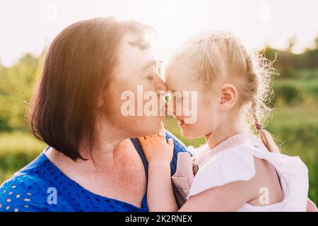 Großmutter hält die Enkelin an den Armen und küsst die Nase Stockfoto