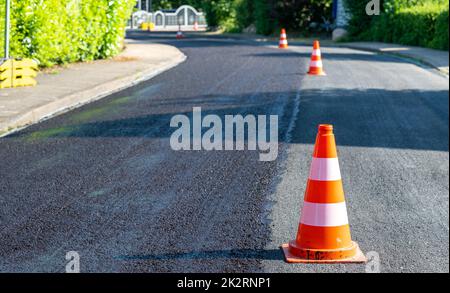 Baukegel markieren einen Teil der Straße mit einer Schicht aus frischem Asphalt. Stockfoto