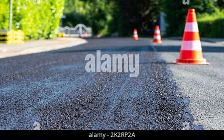 Baukegel markieren einen Teil der Straße mit einer Schicht aus frischem Asphalt. Stockfoto