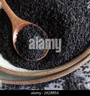 Teller mit indischem Gewürz Schwarzer Kreuzkümmel (Nigella sativa oder Kalonji), Nahaufnahme mit einem Holzlöffel Stockfoto