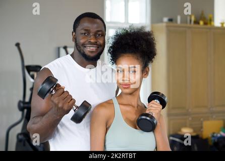 Junge, lockige, schwarze Haare genießen gemeinsam den Urlaub im Fitnesscenter. Beide Hantel mit einer Hand heben. Stockfoto