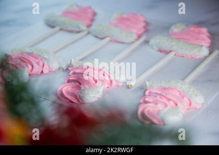 Baiser in Form von pinkfarbenen Weihnachtshüten mit Pompom und weißem Revers auf einem Stock liegen auf weißem Pergament in zwei Reihen Stockfoto