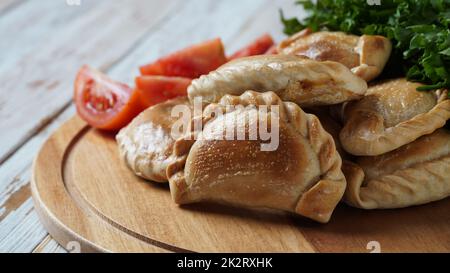 Lateinamerikanische gebratene Empanadas mit Tomatensoße. Argentinian Empanada ist ein Gebäck, das mit einer Vielzahl herzhafter Zutaten gefüllt ist und gebacken oder gebraten wird. Stockfoto