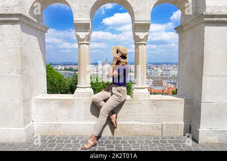 Schöne Frau, die das Stadtbild mit dem ungarischen Parlamentsgebäude und der Donau von der Fischerbastei in Budapest, Ungarn, genießt Stockfoto