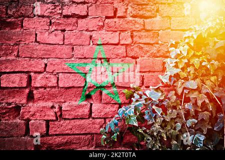 Marokkanische Grunge-Flagge an der Backsteinwand mit Blick auf die Efeu-Pflanze und den Sonnenschirm Stockfoto